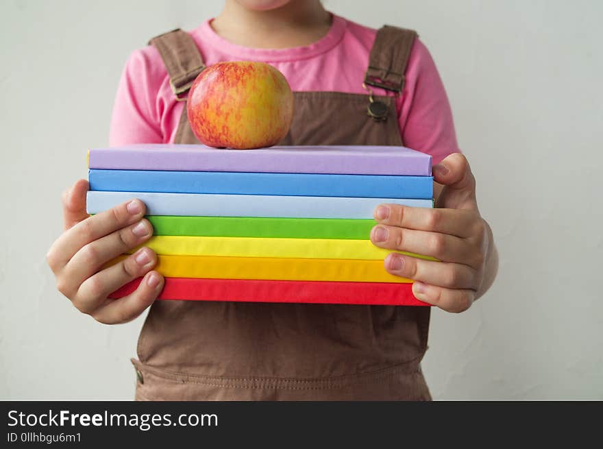 The schoolgirl is holding books and an apple. Hands of the child. Back to school. Life style. A girl in a pink T-shirt is going to learn.