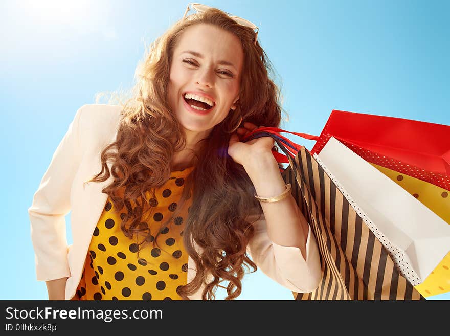 Smiling modern woman with shopping bags against blue sky