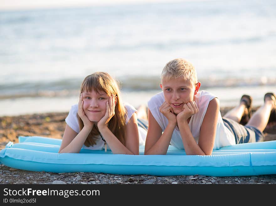 Two children lie on an inflatable mattress, near the sea