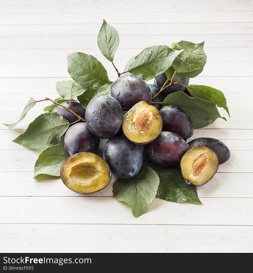 Fresh plum fruit with leaves on a light table.