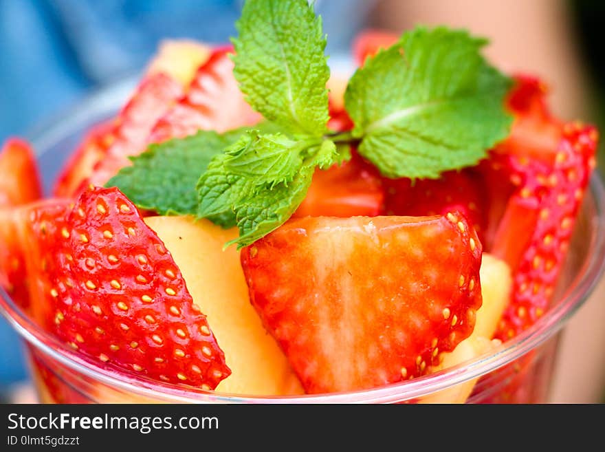 Fresh and fragrant sliced berries and fruits are stacked in a container. Yellow melon and red strawberry. Everything is decorated with a fragrant branch of their several leaves of mint. The fruit is very tasty.