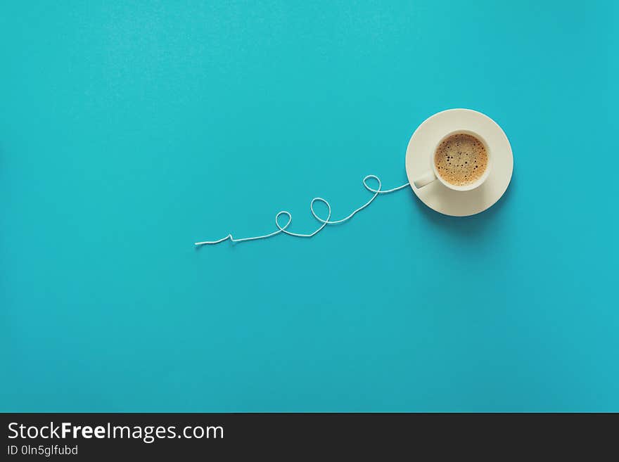 Coffee cup in shape of balloon with clouds on blue paper background. Toned