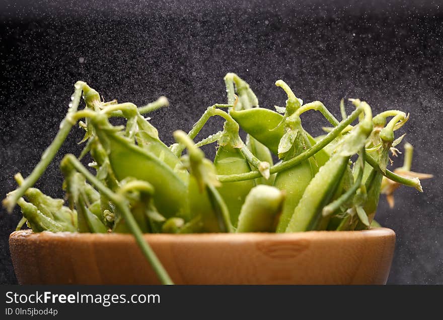 Photo of green pea pods in wooden cup on empty black background in studio