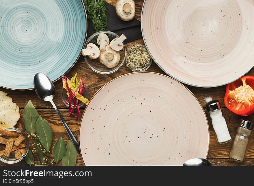 Set of three empty ceramic round plates on wooden table with food ingredients, mockup for meal, top view. Set of three empty ceramic round plates on wooden table with food ingredients, mockup for meal, top view