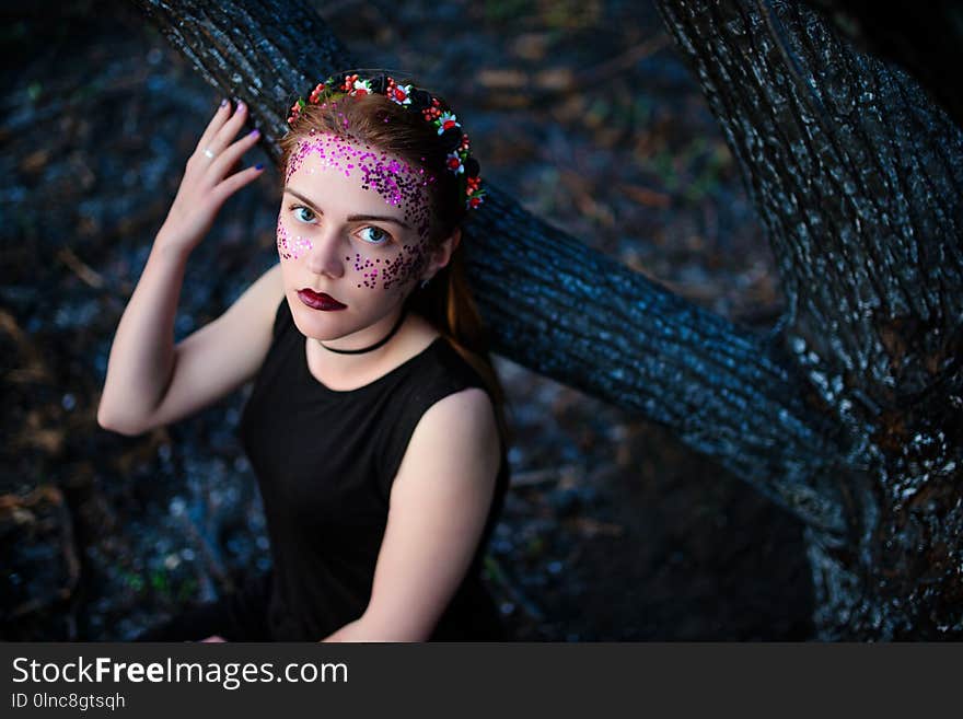 A young beautiful woman with a violet shine on her face stands near a burnt tree.