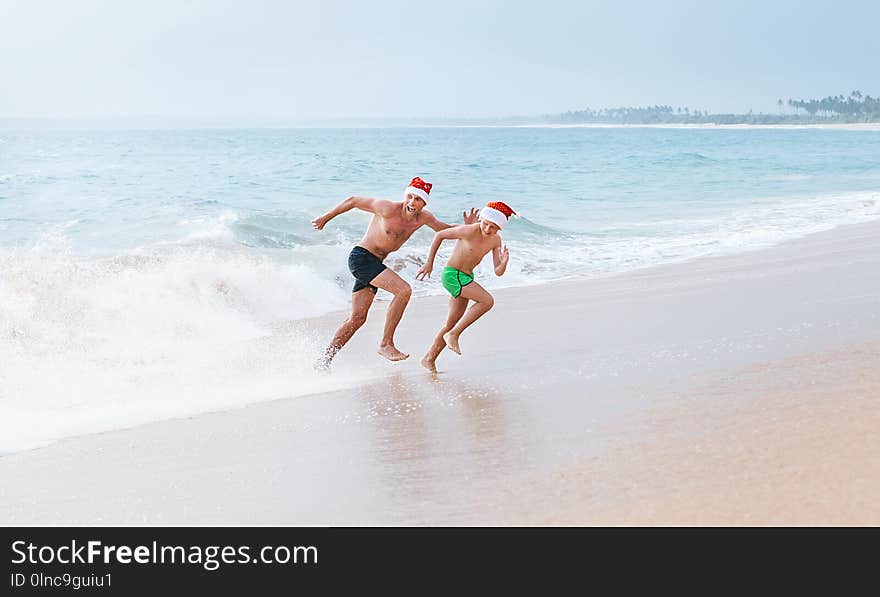 Father and son have a fun on ocean beach, run away from big waves. Christmas holiday time. Tropical vacation