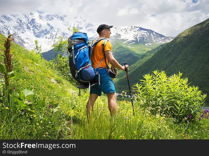 Tourist on a hike in the mountains on a bright sunny day. A young guy with a backpack in a mountainous area on a hiking trail.