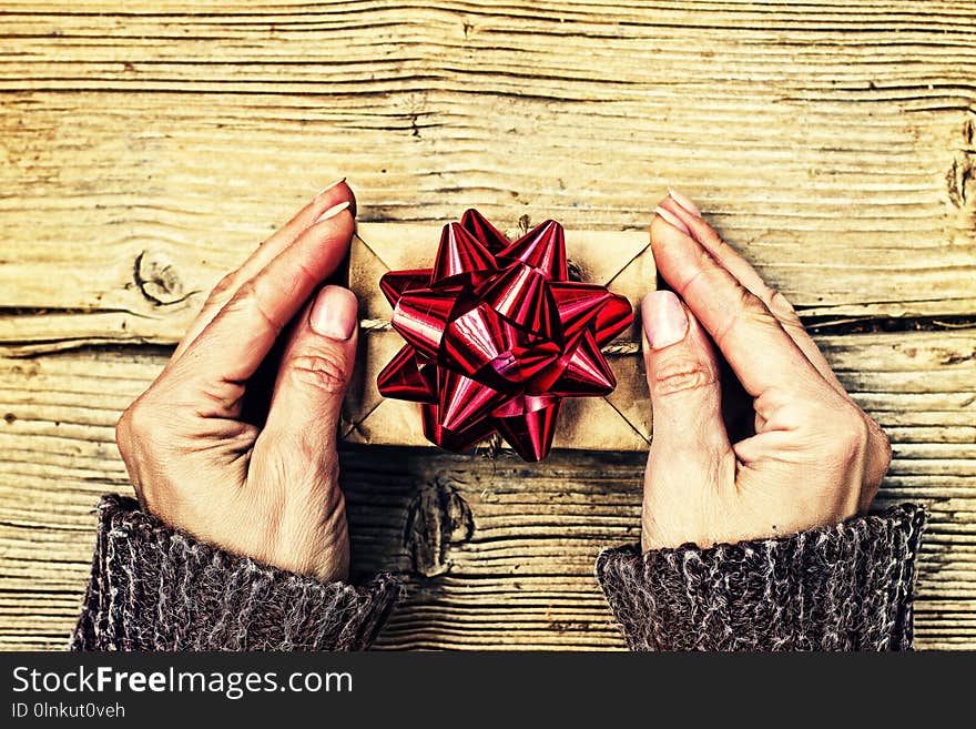 Christmas, Birthday, Valentine`s Day. Gift box with a red bow in female hands on a wooden background, top view. Christmas, Birthday, Valentine`s Day. Gift box with a red bow in female hands on a wooden background, top view