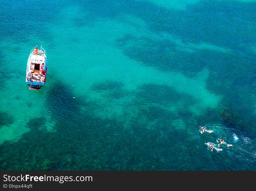 Aerial shot of turquoise water lagoon at hot summer day with white boat. Top view of people swimming around the boat.