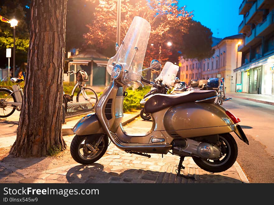 Scooter parked on the sidewalk in night city. Rimini, Italy. Theme of convenient transport.