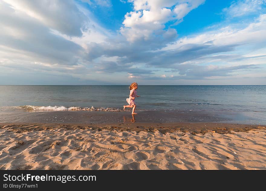 Child on seashore. ttle girl running along seaside in water. Happy kid get fun at the sea.
