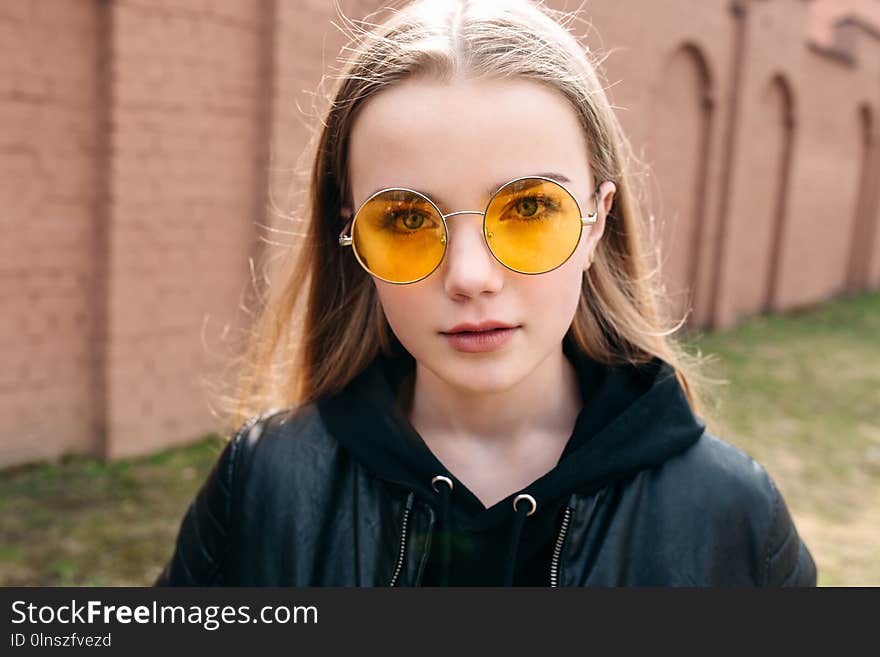 Beautiful fashionable kid girl in yellow sunglasses in city street