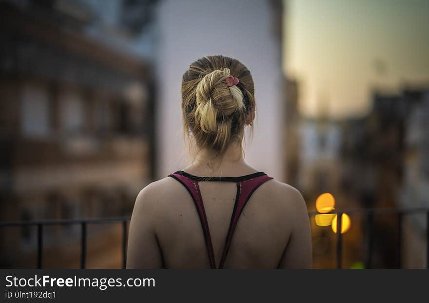 Back of a young woman looking at the cityscape from a terrace at sunset.