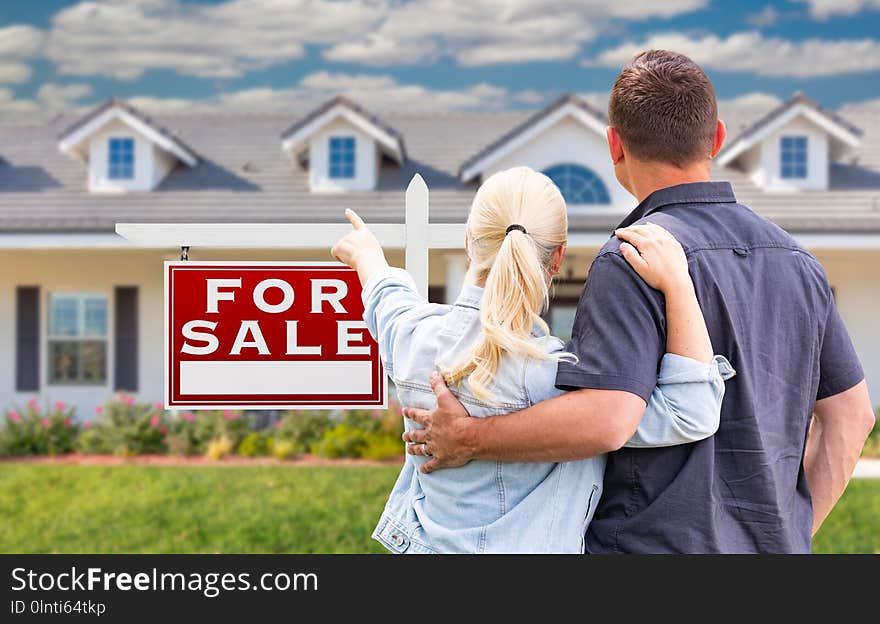 Young Adult Couple Facing and Pointing to Front of For Sale Sign