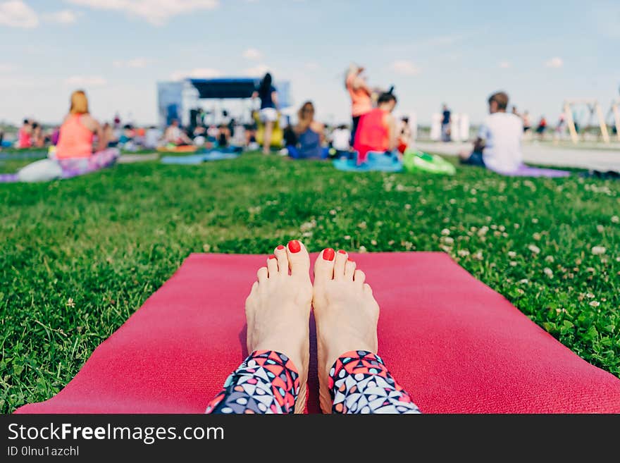 Female feet with red nails on a pink yoga Mat on the grass , a lot of people in the open air at the festival