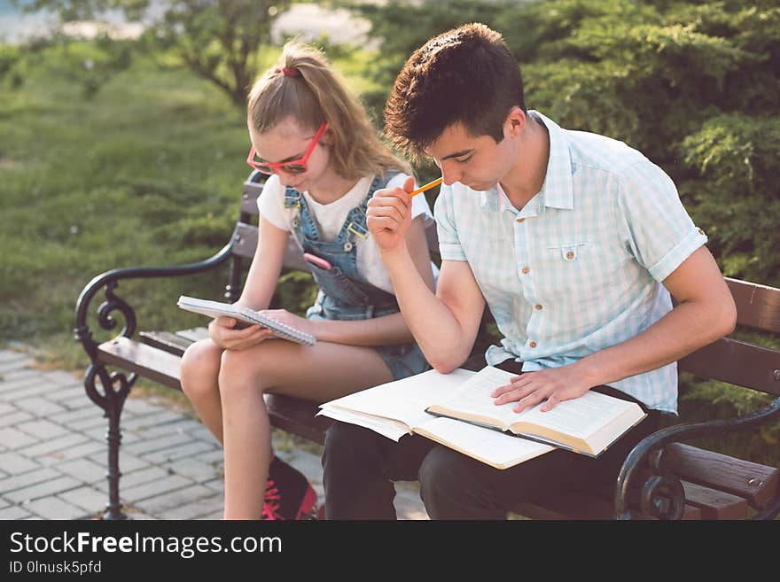 Students learning from books sitting on a bench in a park