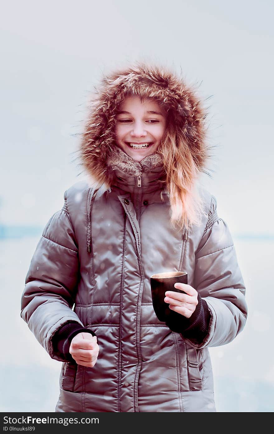 Young pretty smiling girl enjoying drinking hot drink during walk on a wintery day. Wearing coat with hood. Hold a mug of tea. Young pretty smiling girl enjoying drinking hot drink during walk on a wintery day. Wearing coat with hood. Hold a mug of tea