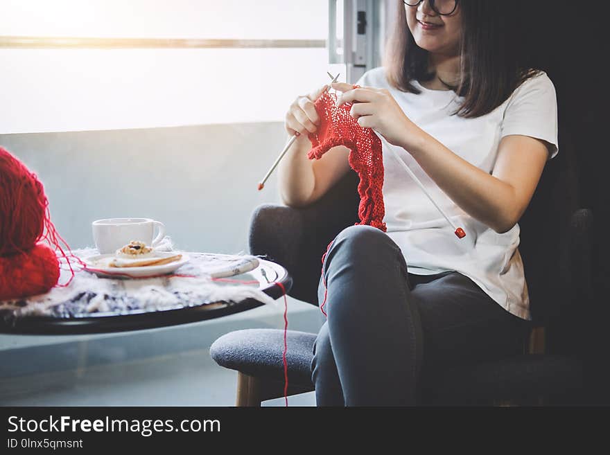 Close up shot of young woman hands knitting a red scarf handicraft in the living room on terrace at home.