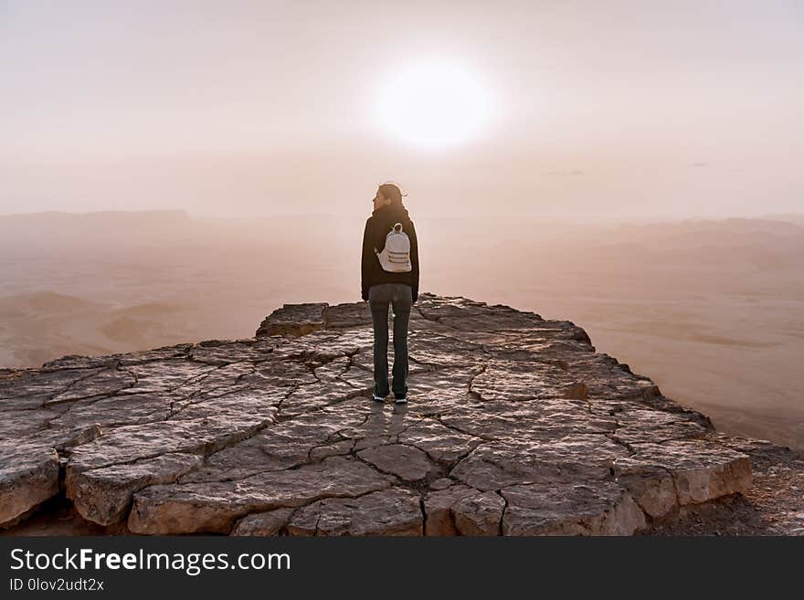 Alone young girl with backpack in israel negev desert admires the view of sunrise. Young female person stands on the edge