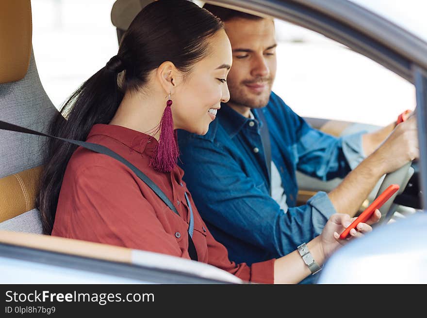 Modern generation. Delighted Asian women using her smartphone while sitting in the car with her boyfriend. Modern generation. Delighted Asian women using her smartphone while sitting in the car with her boyfriend