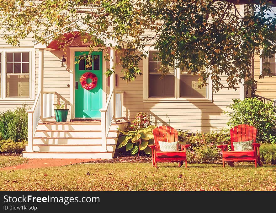 A small cozy wooden traditional American house with wooden chairs by the porch. Autumn sunny day. Vintage style.