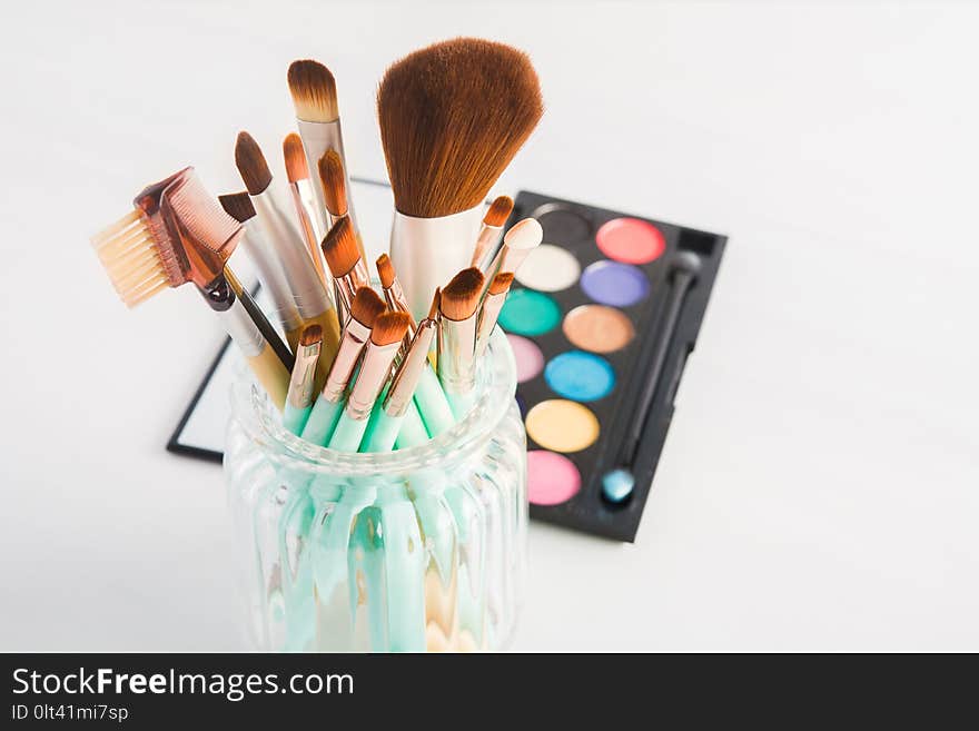 Different makeup brushes in jar on light background, selective focus