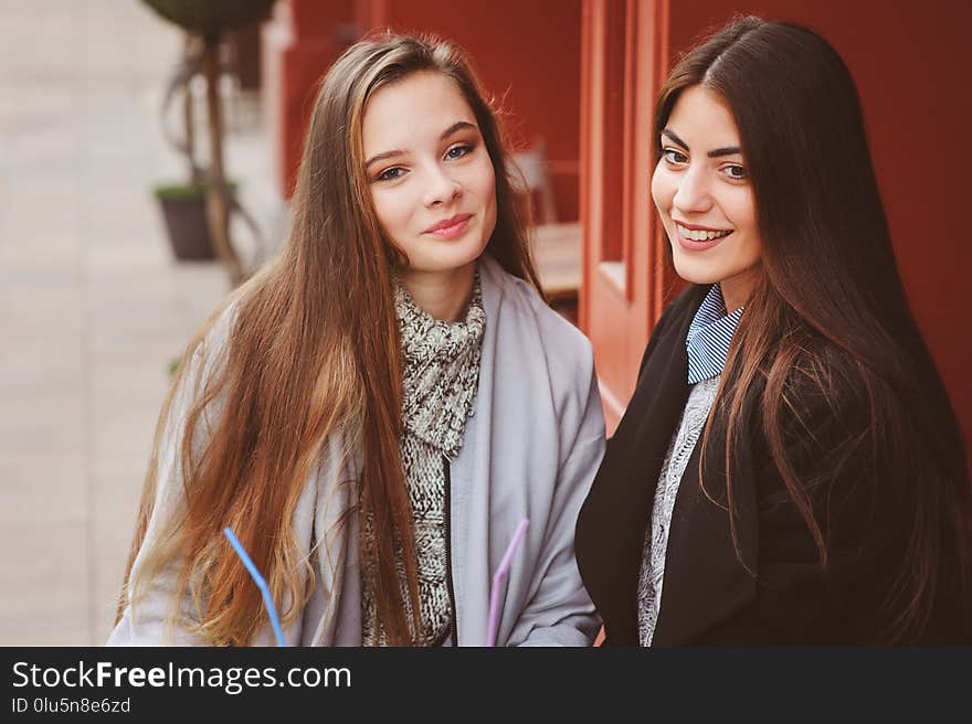 Two happy girl friends talking and drinking coffee in autumn city in cafe. Meeting of good friends, young fashionable students with natural make up.