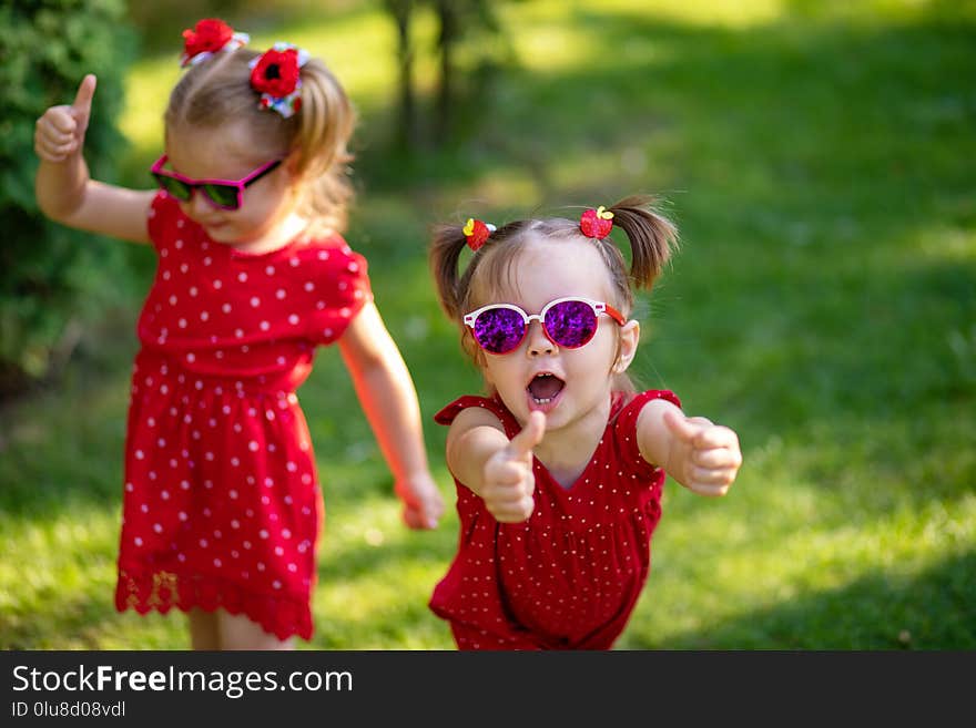 Two cute little girlfriends having fun in the yard. little girl show sight thumbs up and good luck. dressed in bright red dresses