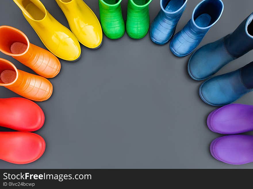 Colorful rubber boots-red, orange, yellow, green, cyan, blue and purple stand in the shape of a rainbow . Top view, space for text.