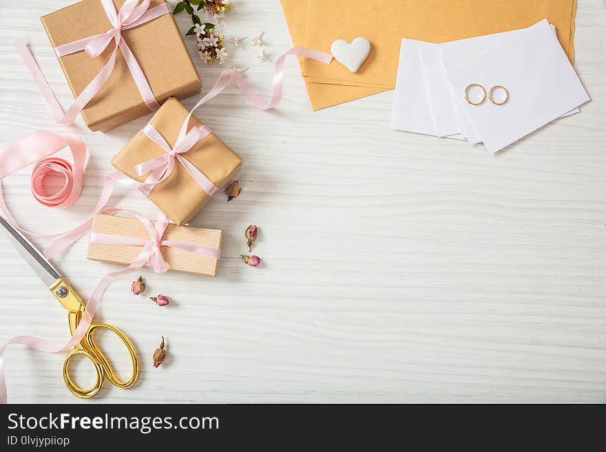Wedding preparation. Flat lay and top view of presents and wedding invitations on a white wooden tabletop, copy space.