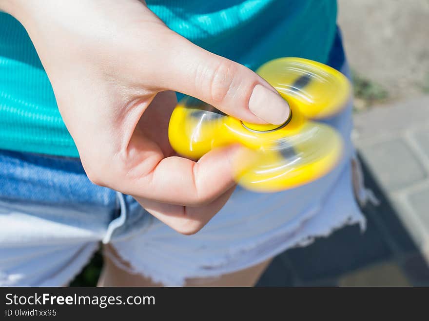 Close up photo of rotating yellow fidget spinner in girl`s hands cropped closeup view photo of teen teenager playing with spinner