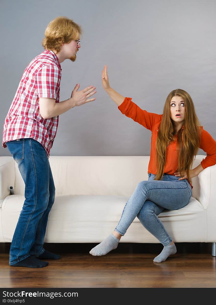 Man begging women who is sitting on sofa for forgiveness. Couple after fight or argue. Female showing speak to hand. Man begging women who is sitting on sofa for forgiveness. Couple after fight or argue. Female showing speak to hand