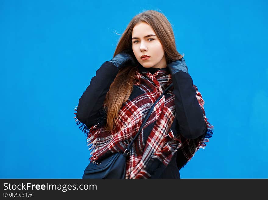 Beautiful woman with a scarf and coat posing near a bright blue wall