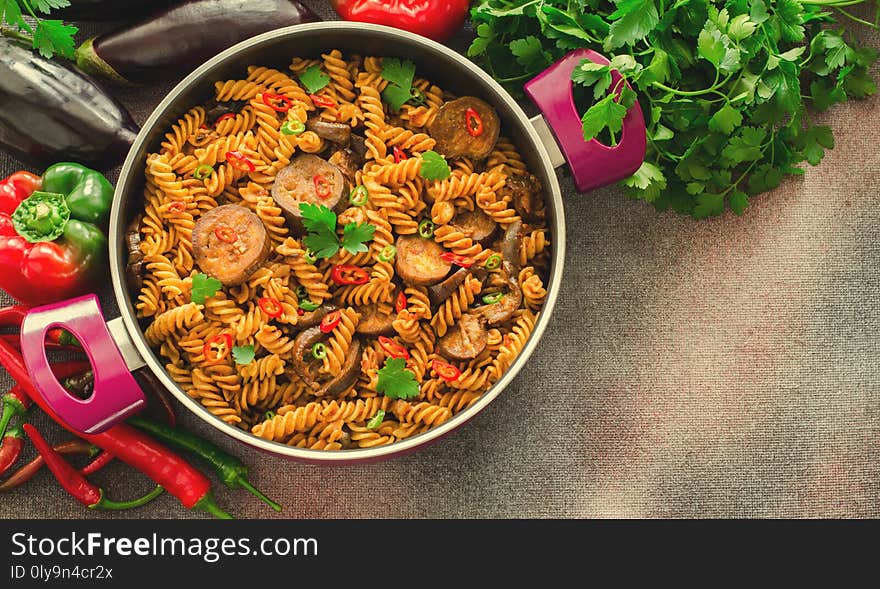 Mediterranean eggplant pasta in pot with tomatoes, red pepper and parsley on grey background. Horizontal, top view, copy space, toned