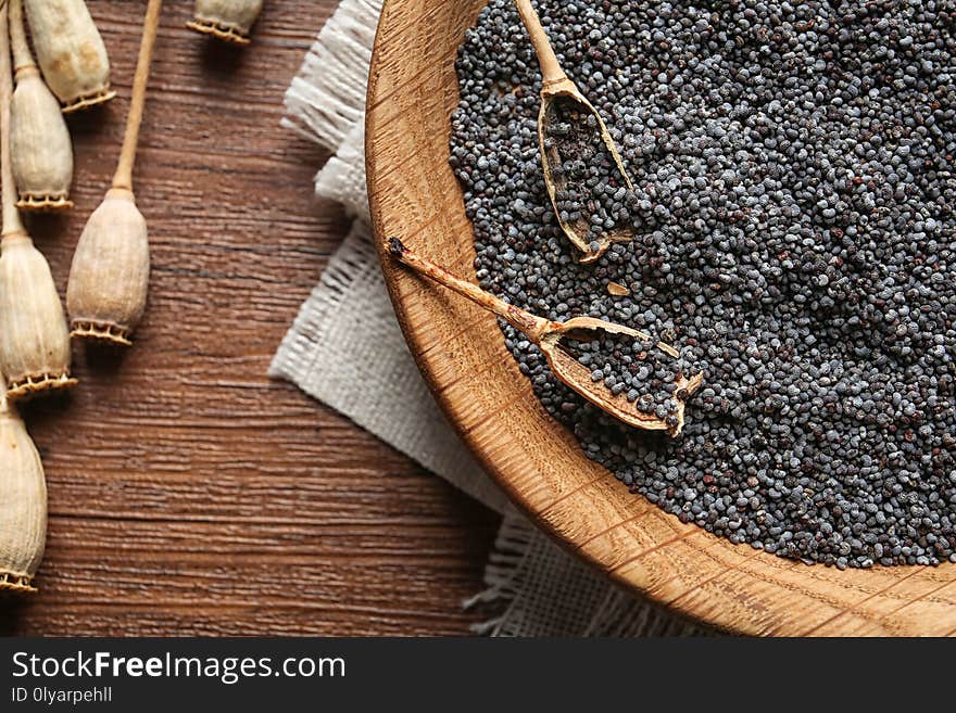 Dry poppy heads and plate with seeds on wooden background, top view