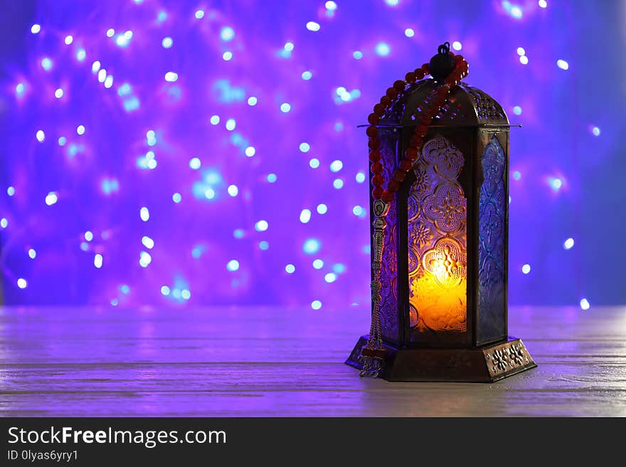 Muslim lamp with candle on table against blurred fairy lights. Fanous as Ramadan symbol