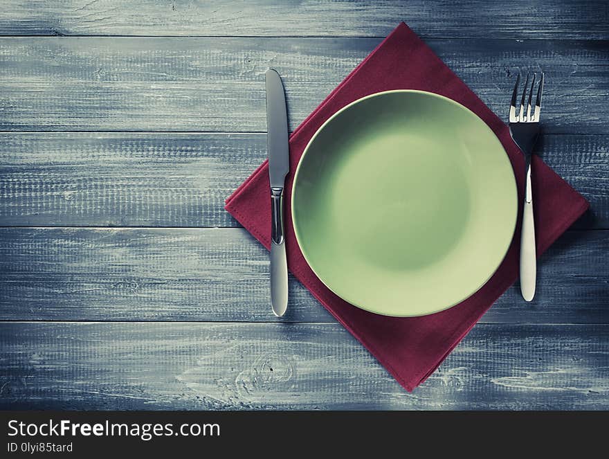 Plate, knife and fork at napkin on wooden background