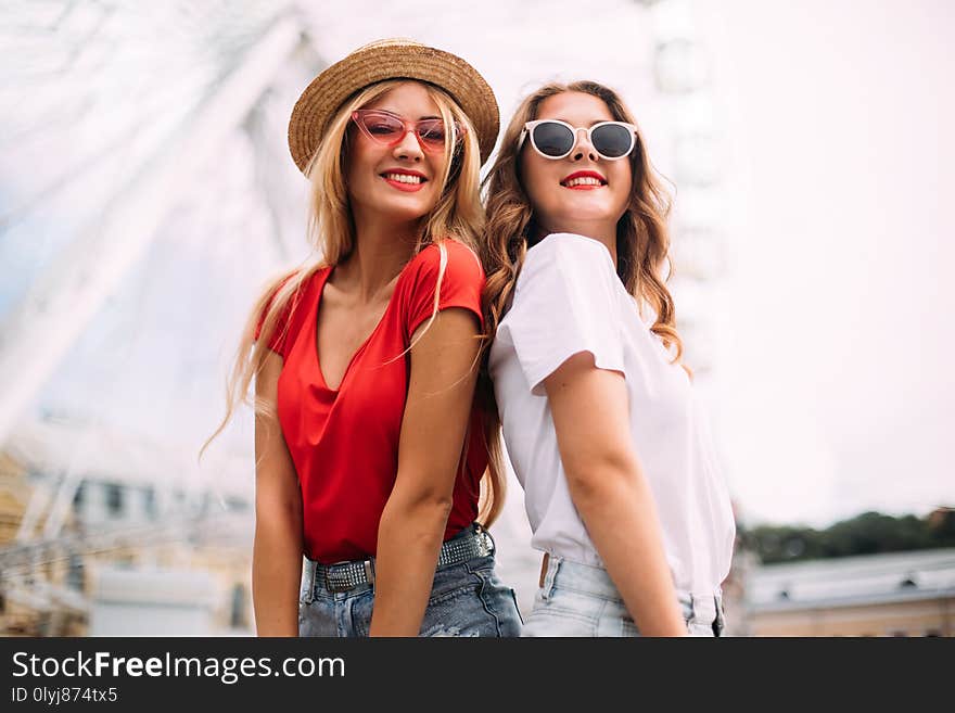 Closeup portrait happy smiling pretty girls having fun.stylishly dressed in short denim shorts and bright t-shirts, sunglasses.posing on the background of a ferris wheel