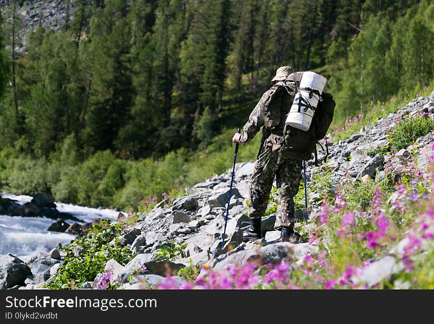 A tourist with a large bag on his back walks along the rocks near a noisy fast river. A tourist with a large bag on his back walks along the rocks near a noisy fast river.