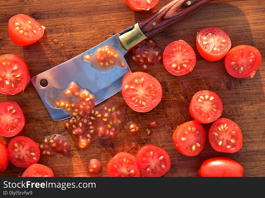 Fresh, ripe grape tomatoes cut into halves on wood cutting board view from above close up details with mini cleaver knife blade full frame photograph. Fresh, ripe grape tomatoes cut into halves on wood cutting board view from above close up details with mini cleaver knife blade full frame photograph