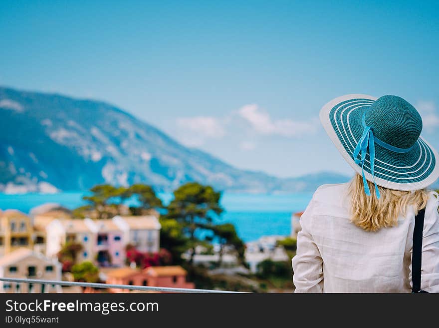 Tourist woman wear blue sunhat and white clothes admire view of colorful tranquil village Assos on sunny day. Stylish