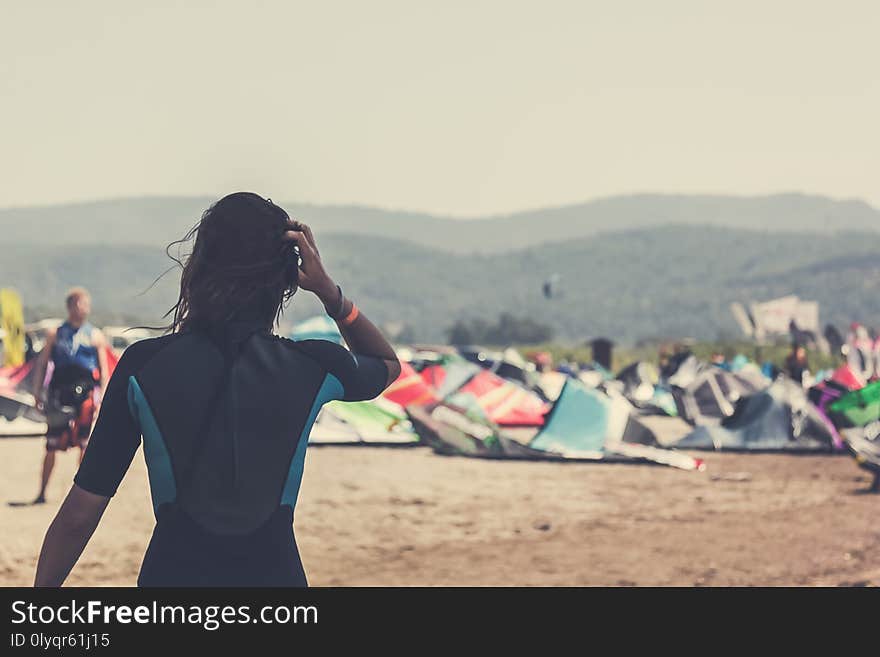 The girl rider is standing and looking into the distance on the laid out kites on the beach on a sunny day