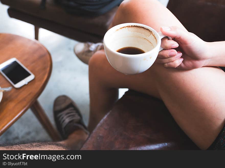 Closeup image of a woman holding black coffee cup while sitting on sofa with friend in cafe