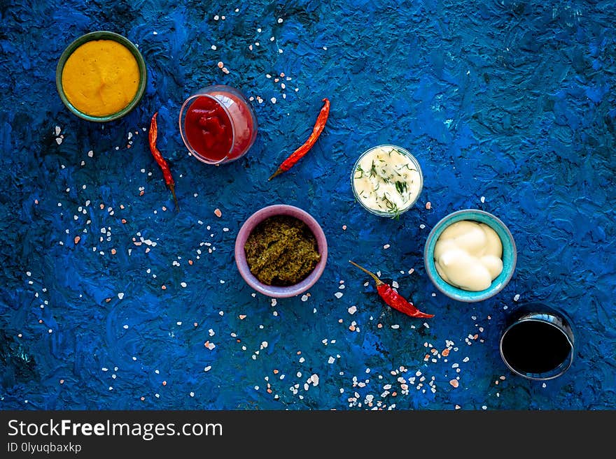 Set of sauces. Ketchup, mayonnaise, mustard, soy sauce, barbecue sauce, pesto, mustard, sour with greenery near chili pepper on blue background top view.