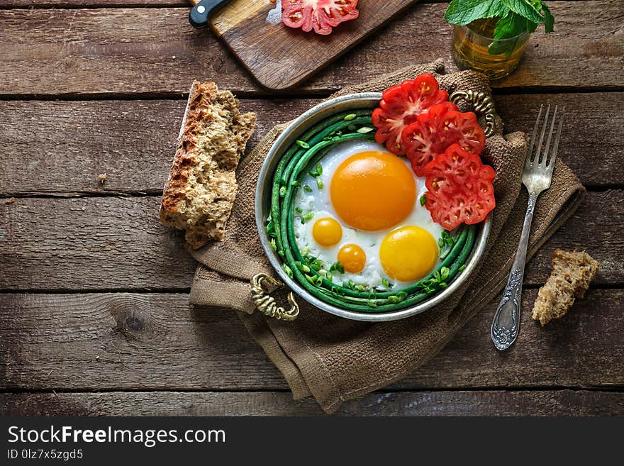 Sunny side fried eggs in a copper pan with tomatoes and green beans, copy space.