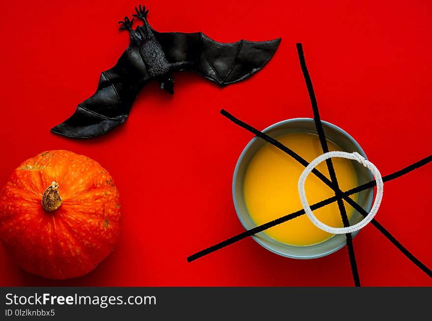 Pumpkin soup in blue bowl isolated on red background, top view. Symbol of HALLOWEEN is black spiderweb and bat , copy space