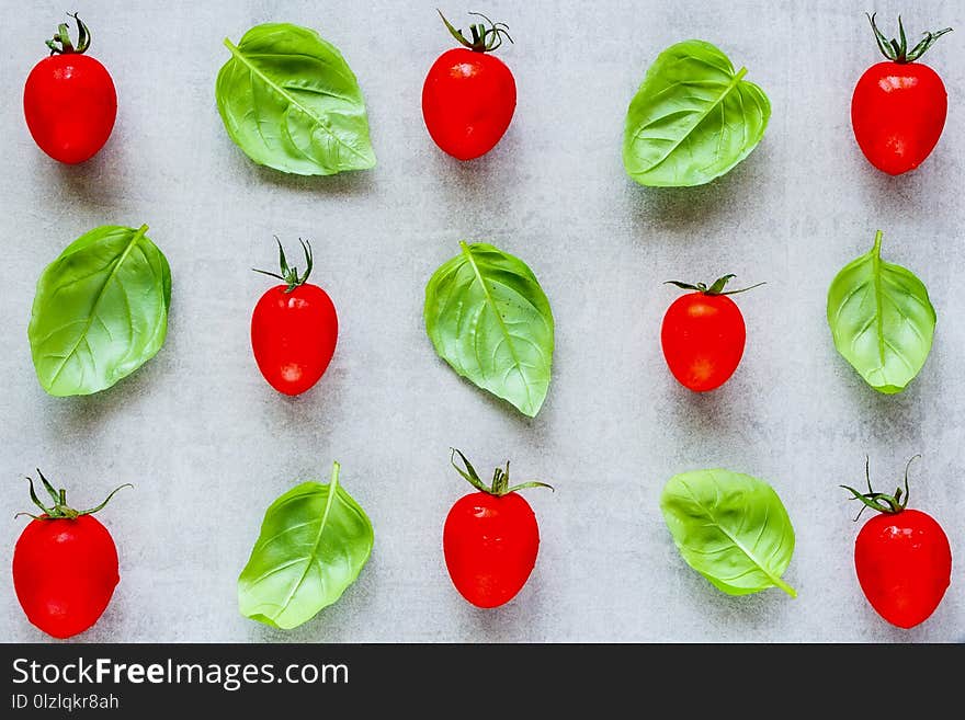 Creative layout made of cherry tomato and basil leaves on light background close up. Ingredients for healthy cooking. Food concept. Flat lay, top view. Creative layout made of cherry tomato and basil leaves on light background close up. Ingredients for healthy cooking. Food concept. Flat lay, top view