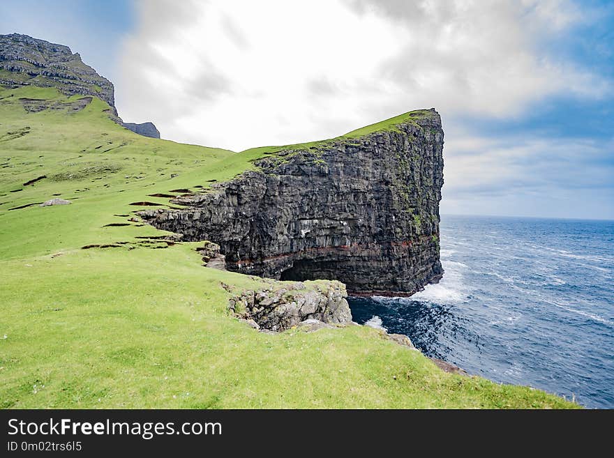 Amazing dramatic view of steep cliff in front of Drangarnir in Vagar island, Faroe Islands, Denmark north Atlantic ocean, best destination for hiking, stunning sea stack with deep blue water.