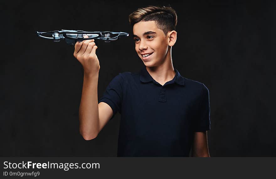 Joyful young guy dressed in a black t-shirt holds a quadcopter. Isolated on the dark background.