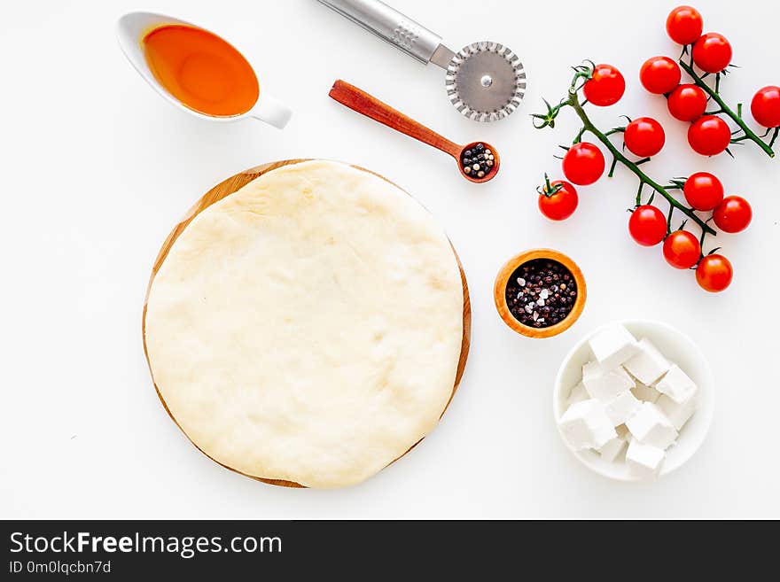 Make pizza concept. Pizza dough and ingredients for filling. Cherry tomatoes, olive oil, cheese mozzarella, spices near knife for pizza on white background top view mockup.